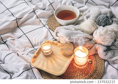 Cozy composition with a cup of tea, a candle and knitted elements on a blanket. Cozy composition with a cup of tea, a candle and knitted elements on a blanket. 137032215