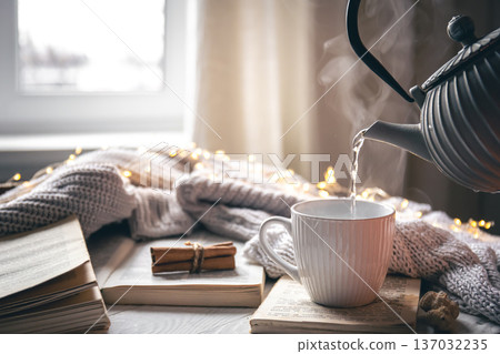Cozy composition with a teapot, a cup and a book on a blurred background. Cozy composition with a teapot, a cup and a book on a blurred background. 137032235