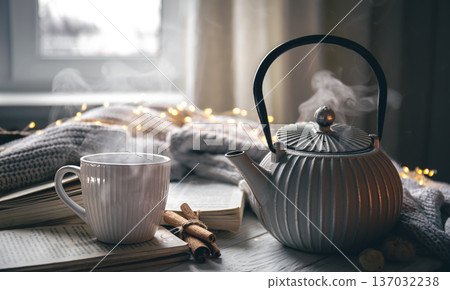 Cozy composition with a teapot, a cup and a book on a blurred background. Cozy composition with a teapot, a cup and a book on a blurred background. 137032238