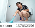 Happy young Asian woman scrubbing bathroom floor with a brush. 137032356