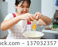Young Asian woman cracking an egg into a bowl in the kitchen. 137032357