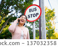 Young Asian woman talking on a smartphone while waiting at a bus stop. 137032358