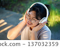 Happy young Asian woman wearing headphones and listening to music. 137032359