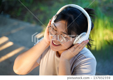 Happy young Asian woman wearing headphones and listening to music. 137032359