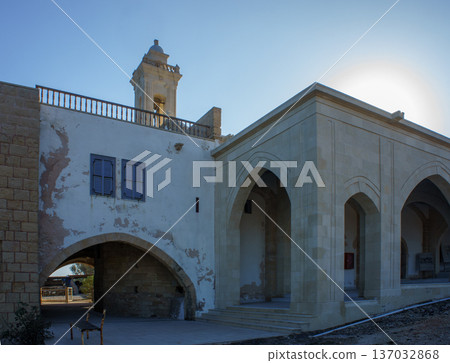 A historic stone building with arched architecture under a bright sky at sunset. 137032868