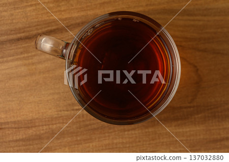 A warm cup of black tea resting on a wooden table, inviting tranquility during a quiet afternoon A warm cup of black tea resting on a wooden table, inviting tranquility during a quiet afternoon 137032880