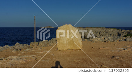 A solitary rock emerges against the vast blue sea under a clear sky at sunset on a tranquil shoreline. A solitary rock emerges against the vast blue sea under a clear sky at sunset on a tranquil shoreline. 137032895