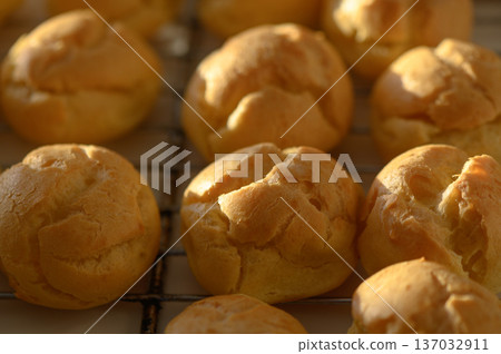 Golden pastry puffs freshly baked and cooling on a wire rack in a warm kitchen Golden pastry puffs freshly baked and cooling on a wire rack in a warm kitchen 137032911