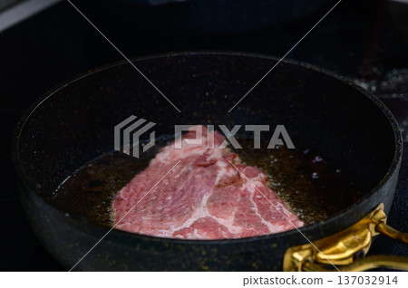 Sizzling beef steak heating in a black frying pan on a modern kitchen stovetop during evening preparation Sizzling beef steak heating in a black frying pan on a modern kitchen stovetop during evening preparation 137032914