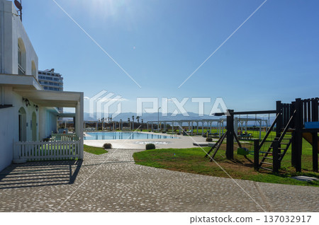 A serene afternoon at a coastal resort featuring a pool and playground under a clear blue sky. A serene afternoon at a coastal resort featuring a pool and playground under a clear blue sky. 137032917