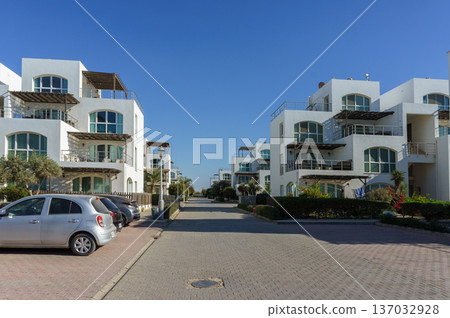 Modern coastal residences line the tranquil street on sunny day near the shore. 137032928