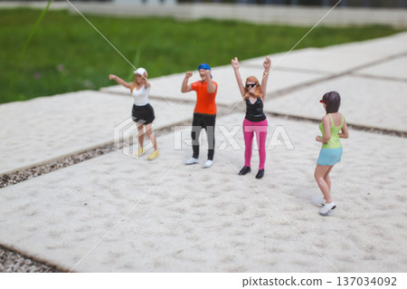 Miniature dancers raise arms energetically on outdoor concrete surface 137034092