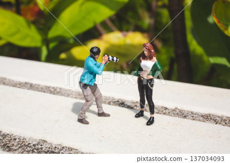 Miniature photographer captures model posing beside green foliage Miniature photographer captures model posing beside green foliage 137034093