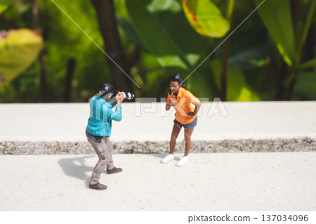 Miniature photographer captures model posing beside green foliage Miniature photographer captures model posing beside green foliage 137034096