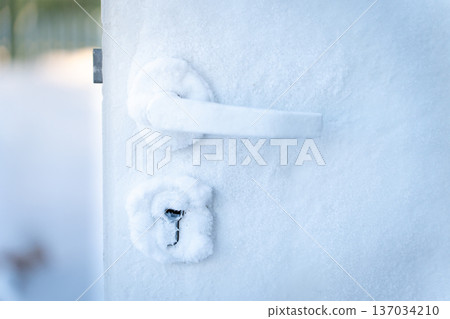A frozen door handle and lock covered in frost during severe winter conditions. Close-up view of ice-covered doors illustrating house freezing from the inside. Perfect for concepts of cold weather 137034210