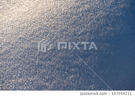 Texture of snow in warm sunlight, creating a beautiful frozen nature background. The soft winter light highlights the delicate crystalline structure and pristine white surface. 137034211