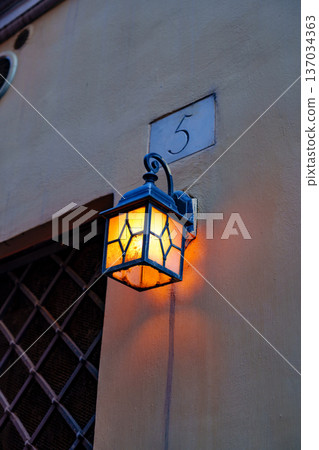 Lamp shines on wall near house number five in evening light 137034363