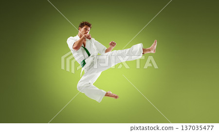 Young karate athlete delivering powerful side kick in mid air wearing white gi and green belt. Young karate athlete delivering powerful side kick in mid air wearing white gi and green belt. 137035477
