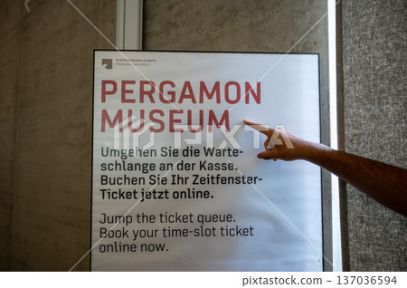 Berlin, germany, august 16, 2023. A hand pointing at a sign indicating the pergamon museum, offering information about booking time-slot tickets online in berlin Berlin, germany, august 16, 2023. A hand pointing at a sign indicating the pergamon museum, offering information about booking time-slot tickets online in berlin 137036594