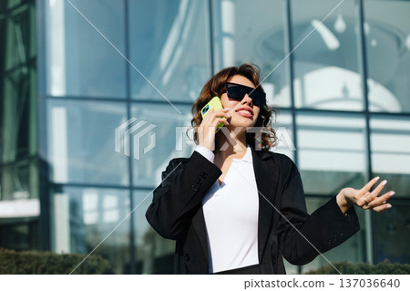 Businesswoman gesturing while speaking on phone in modern city environment Businesswoman gesturing while speaking on phone in modern city environment 137036640