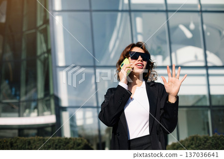 Expressive businesswoman talking on phone and gesturing outdoors Expressive businesswoman talking on phone and gesturing outdoors 137036641