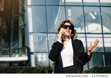 Confident Businesswoman Talking On Smartphone Near Glass Office Building 137036642