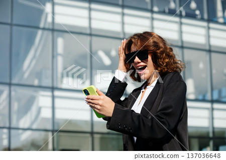 Stylish Businesswoman Holding Smartphone Near Modern Office Building 137036648