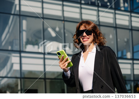 Smiling Businesswoman Using Smartphone In Urban Corporate Environment 137036653