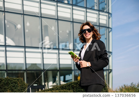 Happy Businesswoman Talking On Phone And Smiling In Sunlight Outdoors Happy Businesswoman Talking On Phone And Smiling In Sunlight Outdoors 137036656