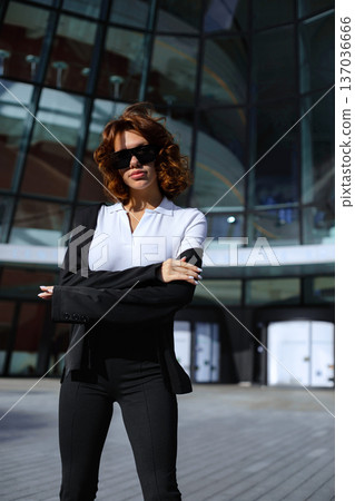Smiling Businesswoman Adjusting Sunglasses Near Modern Office Building 137036666