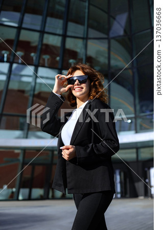 Stylish Businesswoman Looking Away Near Modern Office Glass Building Stylish Businesswoman Looking Away Near Modern Office Glass Building 137036668