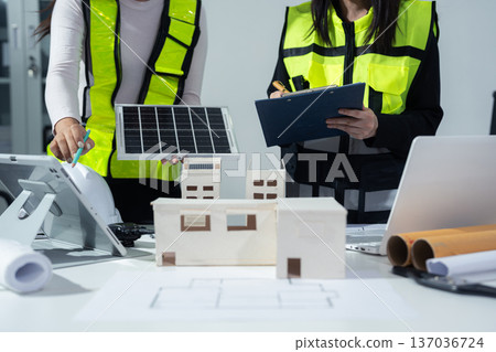Two colleagues discussing data working and tablet, laptop with on Construction Site project, green energy and solar panel concept. 137036724