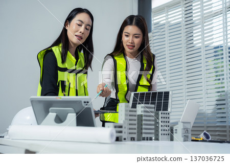Two colleagues discussing data working and tablet, laptop with on Construction Site project, green energy and solar panel concept. 137036725