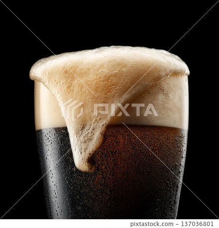 Foamy dark stout beer in a pint glass with creamy foam head, isolated on black background, concept of refreshment and taste Foamy dark stout beer in a pint glass with creamy foam head, isolated on black background, concept of refreshment and taste 137036801