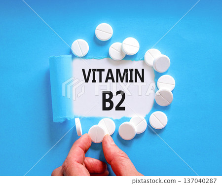 Vitamin B2 riboflavin symbol. Concept words Vitamin B2 on beautiful white paper. White pills tablets. Doctor's hand. Beautiful blue background. Medical healthy lifestyle Vitamin B2 riboflavin concept. Vitamin B2 riboflavin symbol. Concept words Vitamin B2 on beautiful white paper. White pills tablets. Doctor's hand. Beautiful blue background. Medical healthy lifestyle Vitamin B2 riboflavin concept. 137040287