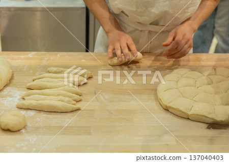 Baker shaping dough on wooden countertop with various bread forms and flour scattered around 137040403