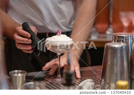 Bartender preparing cocktail with foam and garnish in stylish bar setting Bartender preparing cocktail with foam and garnish in stylish bar setting 137040410