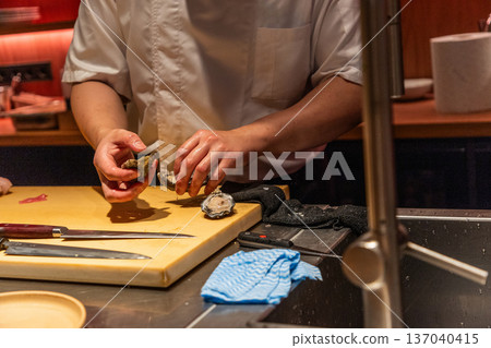 Chef preparing fresh oysters on wooden cutting board in modern kitchen 137040415