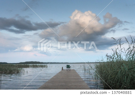 A peaceful evening on the lake side with pier. Lush green grass covers the shoreline, leading the eye to scenic expanse of blue water meeting a sky filled with soft clouds at the horizon classic A peaceful evening on the lake side with pier. Lush green grass covers the shoreline, leading the eye to scenic expanse of blue water meeting a sky filled with soft clouds at the horizon classic 137040881