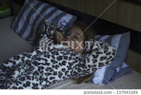 a girl in a terry robe lies on a pillow. child smiles and looks away a girl in a terry robe lies on a pillow. child smiles and looks away 137041089