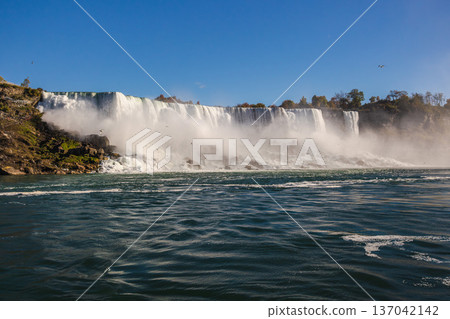 Niagara Falls powerful waterfall landscape with mist and flowing water under clear blue sky Niagara Falls powerful waterfall landscape with mist and flowing water under clear blue sky 137042142