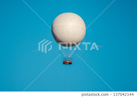 White observation balloon flying in blue sky with suspended passenger gondola White observation balloon flying in blue sky with suspended passenger gondola 137042144