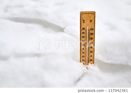 Wooden thermometer measuring freezing temperature in snow 137042361