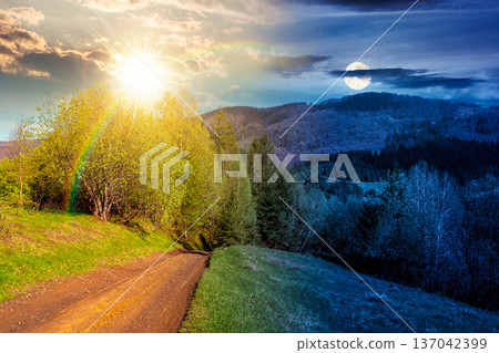 beautiful mountain landscape with dirt road. day meet night. sun and moon over forest path through grassy hills in spring. rural transportation in greenery scenery. empty straight trail near pasture 137042399