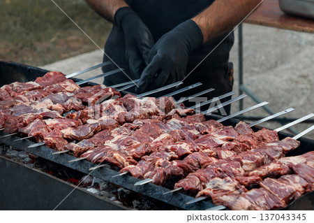 Raw meat skewers on barbecue grill with chef hands 137043345