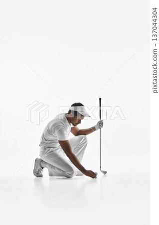 Golfer kneeling and placing ball on tee on white background. Golfer kneeling and placing ball on tee on white background. 137044304