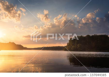 Amazing sunrise over lake with colorful clouds at the horizon. Forest on the lake side. Sunny morning in wild nature. 137044385