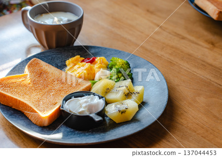 木桌上擺著一盤早餐，包括吐司、炒蛋、奇異果和湯。 137044453