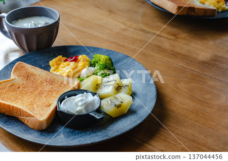Breakfast set on a wooden table: toast, scrambled eggs and kiwi on a plate Breakfast set on a wooden table: toast, scrambled eggs and kiwi on a plate 137044456