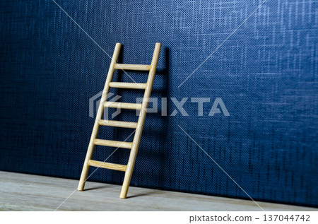 Wooden ladder leaning on deep blue cover with customizable space for text or ideas 137044742